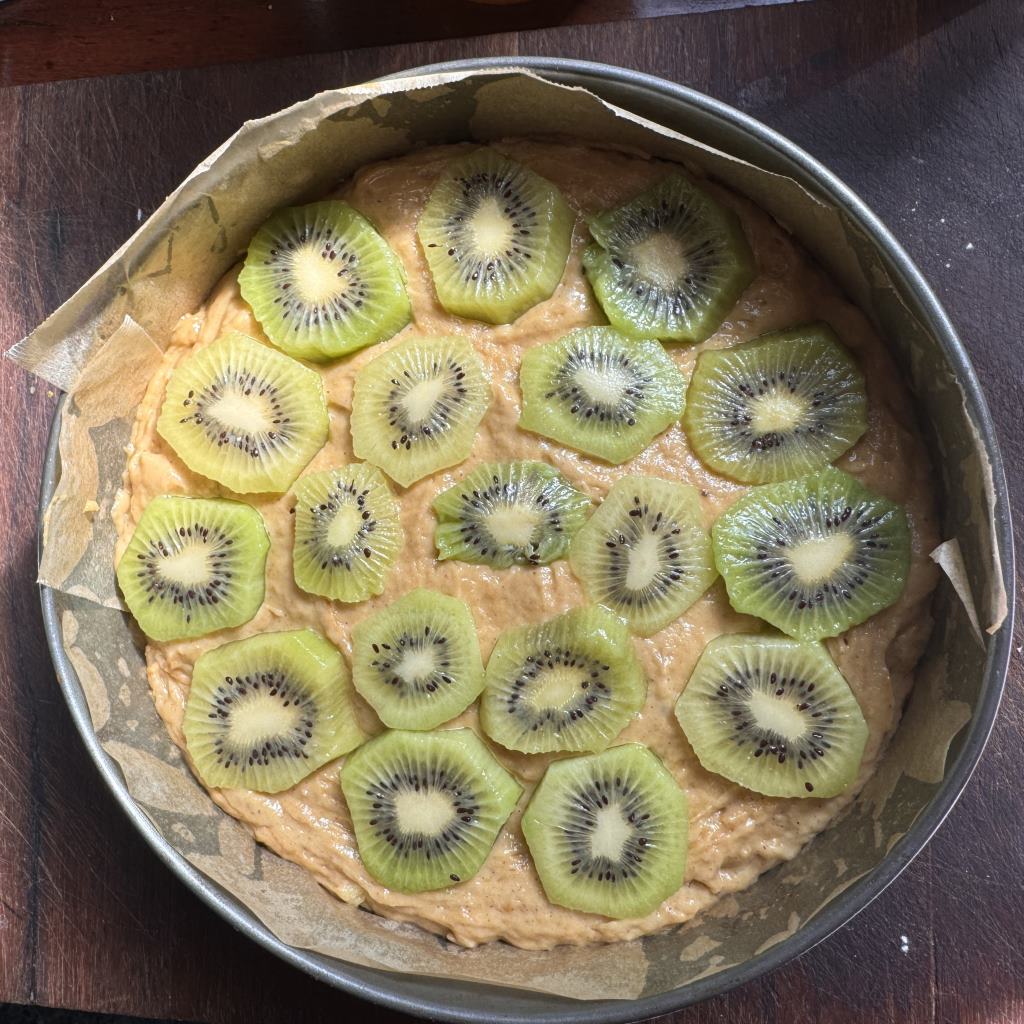 Spring form pan lined with baking paper, the gluten free cake batter is topped with slices of kiwi fruit